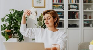 Woman working on computer with money in hand.